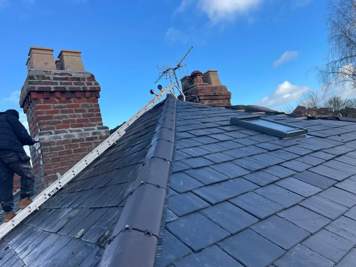 Tradesman carrying out pitched slate roof repairs beside a brick chimney stack in Worcester