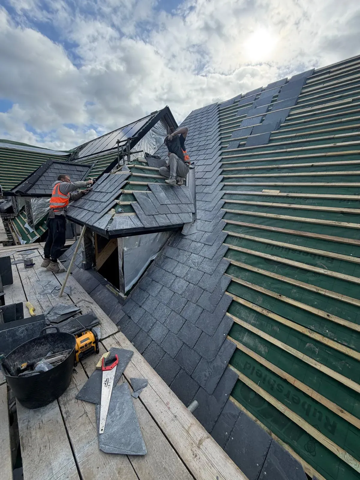 Roofers installing natural slate onto timber battens and breathable underlay on a pitched roof
