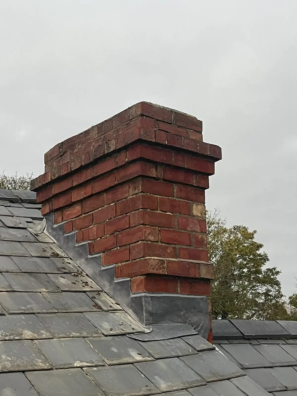 Red-brick chimney stack with stepped lead flashing on a slate roof