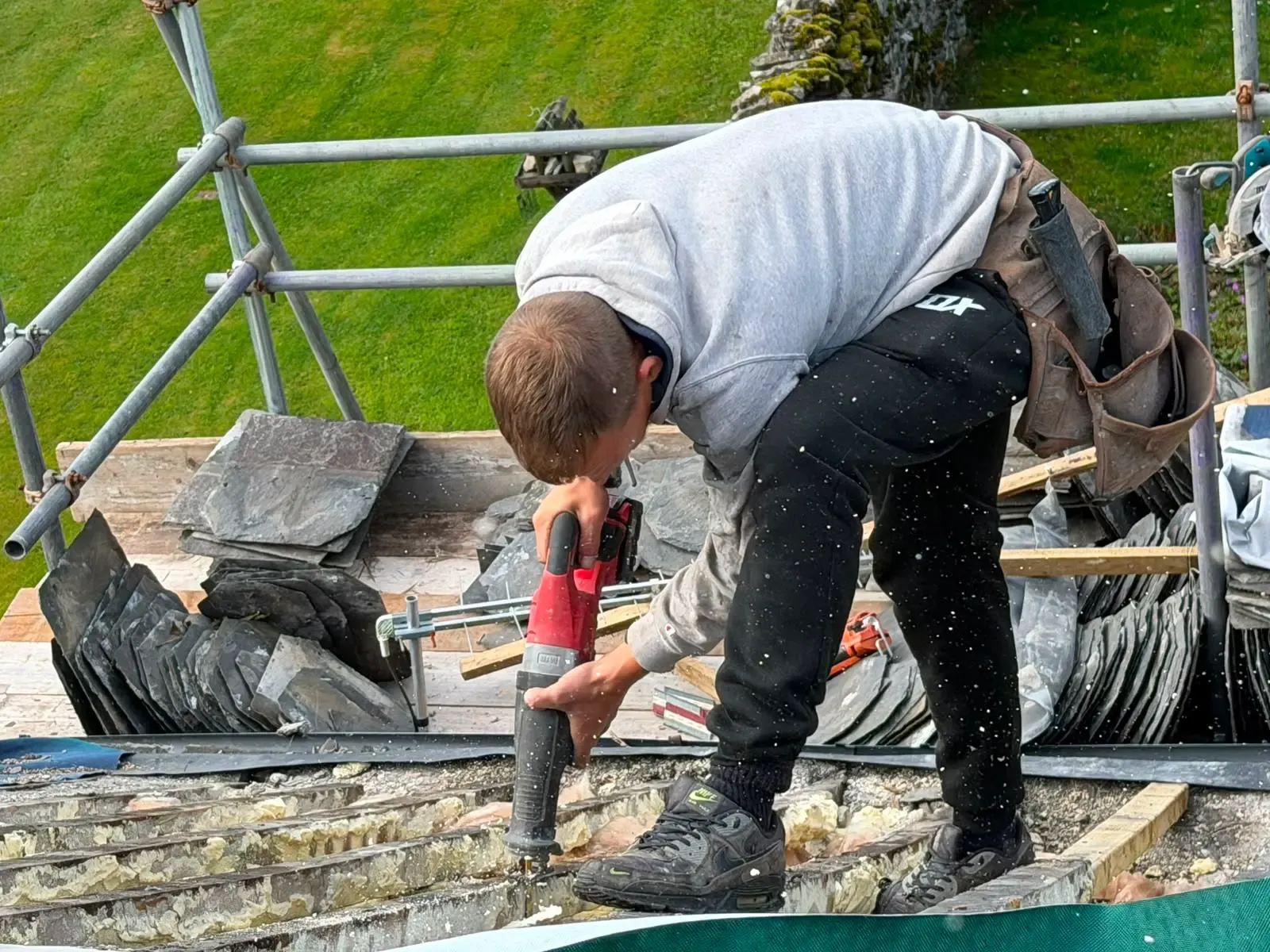 Roofer carrying out timber rafter works and spray foam insulation extraction on a slate roof renovation