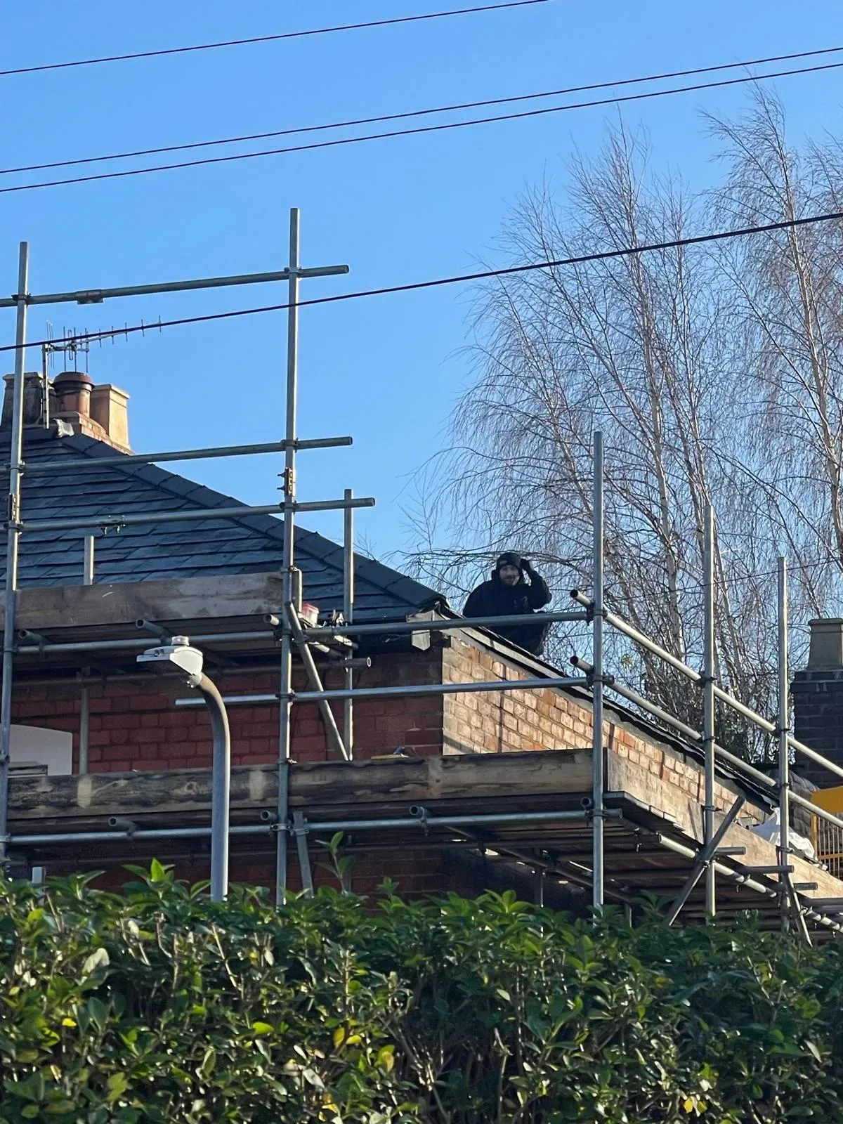 Roofer carrying out repairs on a pitched slate roof supported by scaffolding on a brick property
