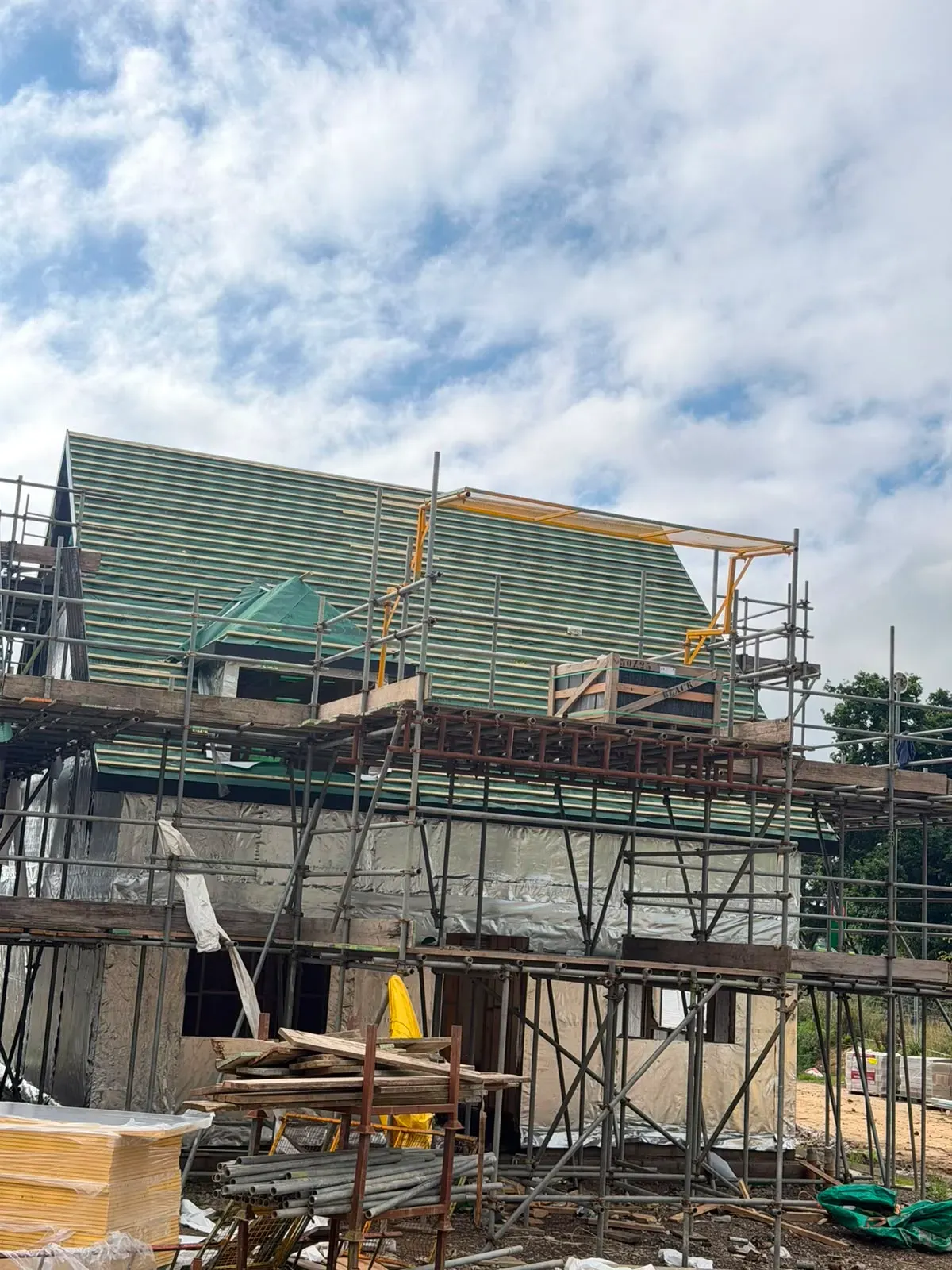 Pitched roof under construction with timber battens and roofing underlay installed on a scaffolded house