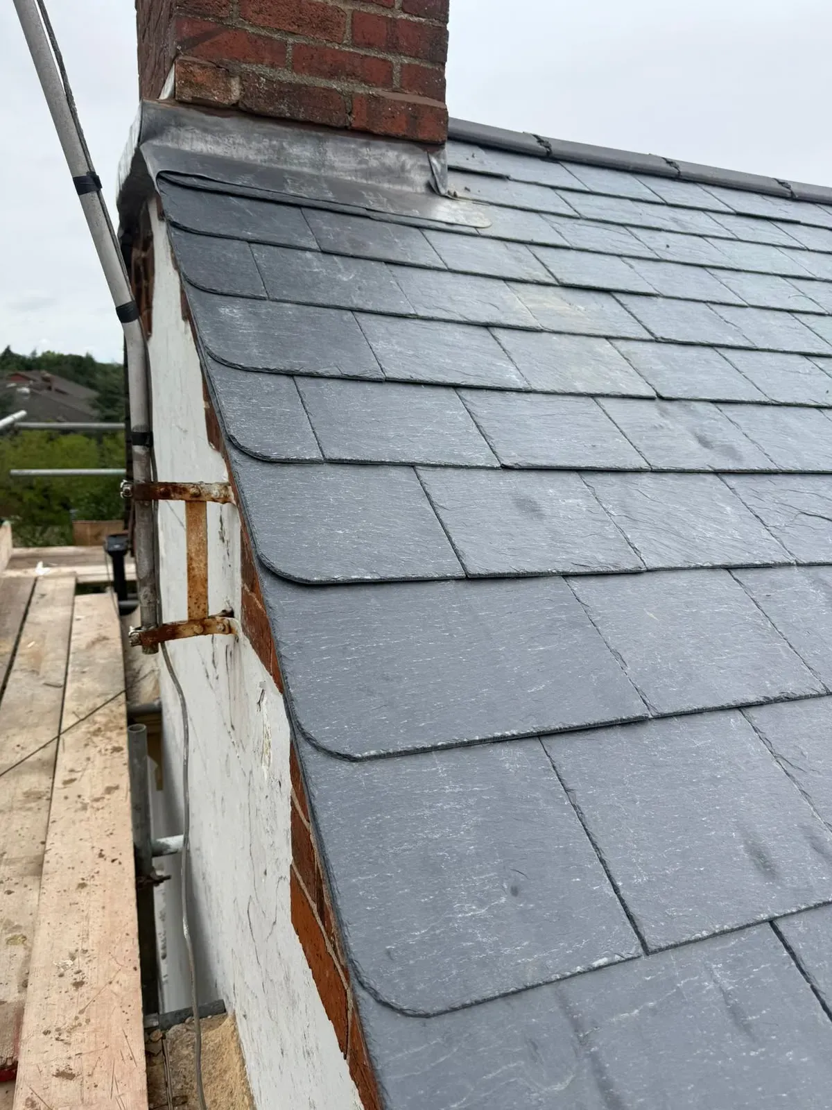 Finished natural slate roof installation showing precision cut verge slates and lead flashing beside a chimney stack in Worcester