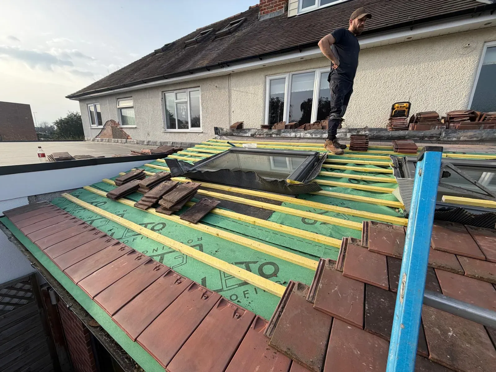 Roofer installing breathable underlay, timber battens, and clay tiles on a pitched lean-to roof extension