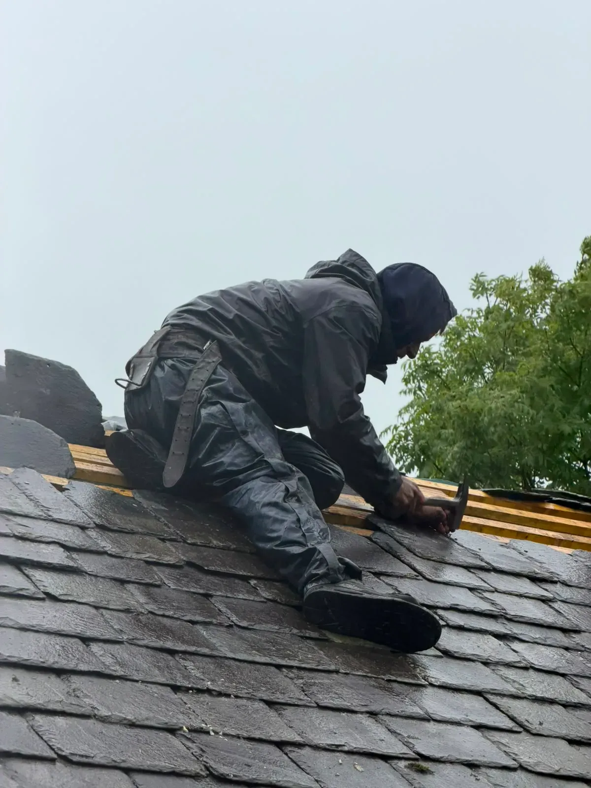 Roofer fixing natural slate tiles on timber battens during roof repair work in Worcester