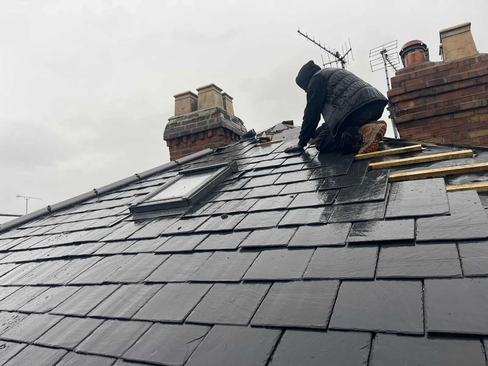 Roofer fixing natural slate roof tiles on a pitched domestic roof with chimney stacks in Worcester