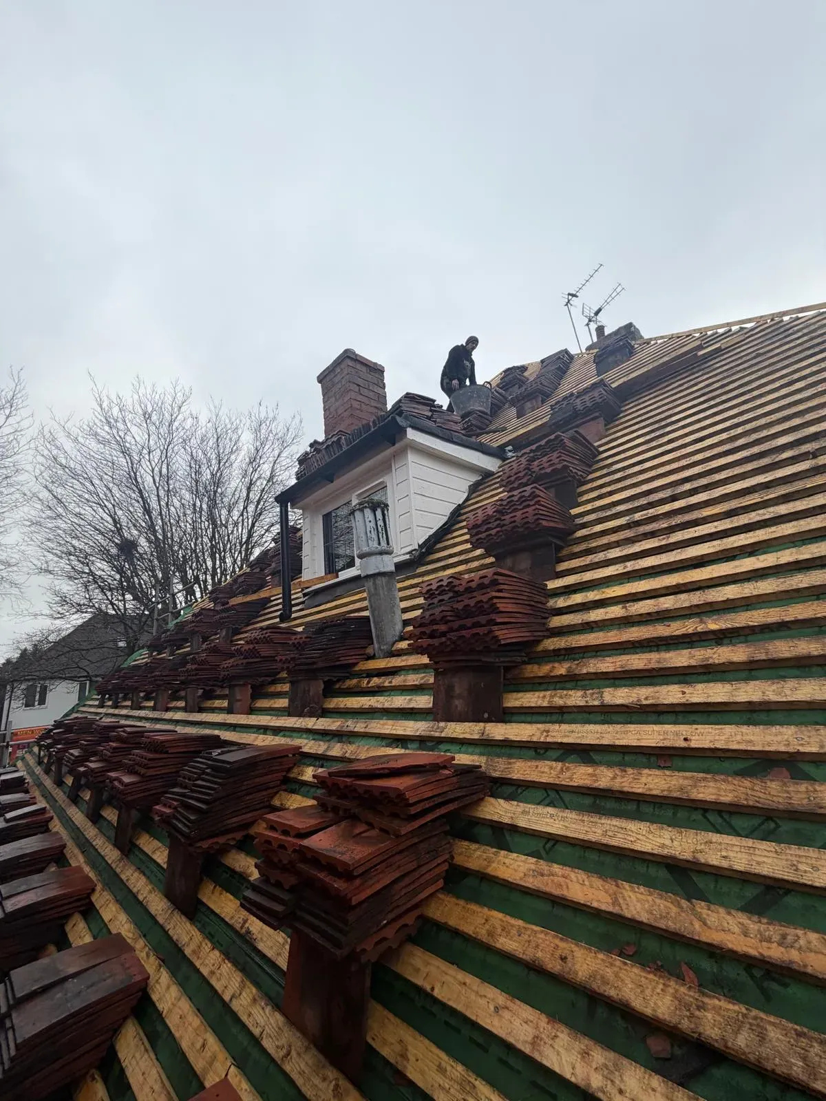 Pitched roof installation in progress with timber battens, breathable membrane, and stacked roof tiles
