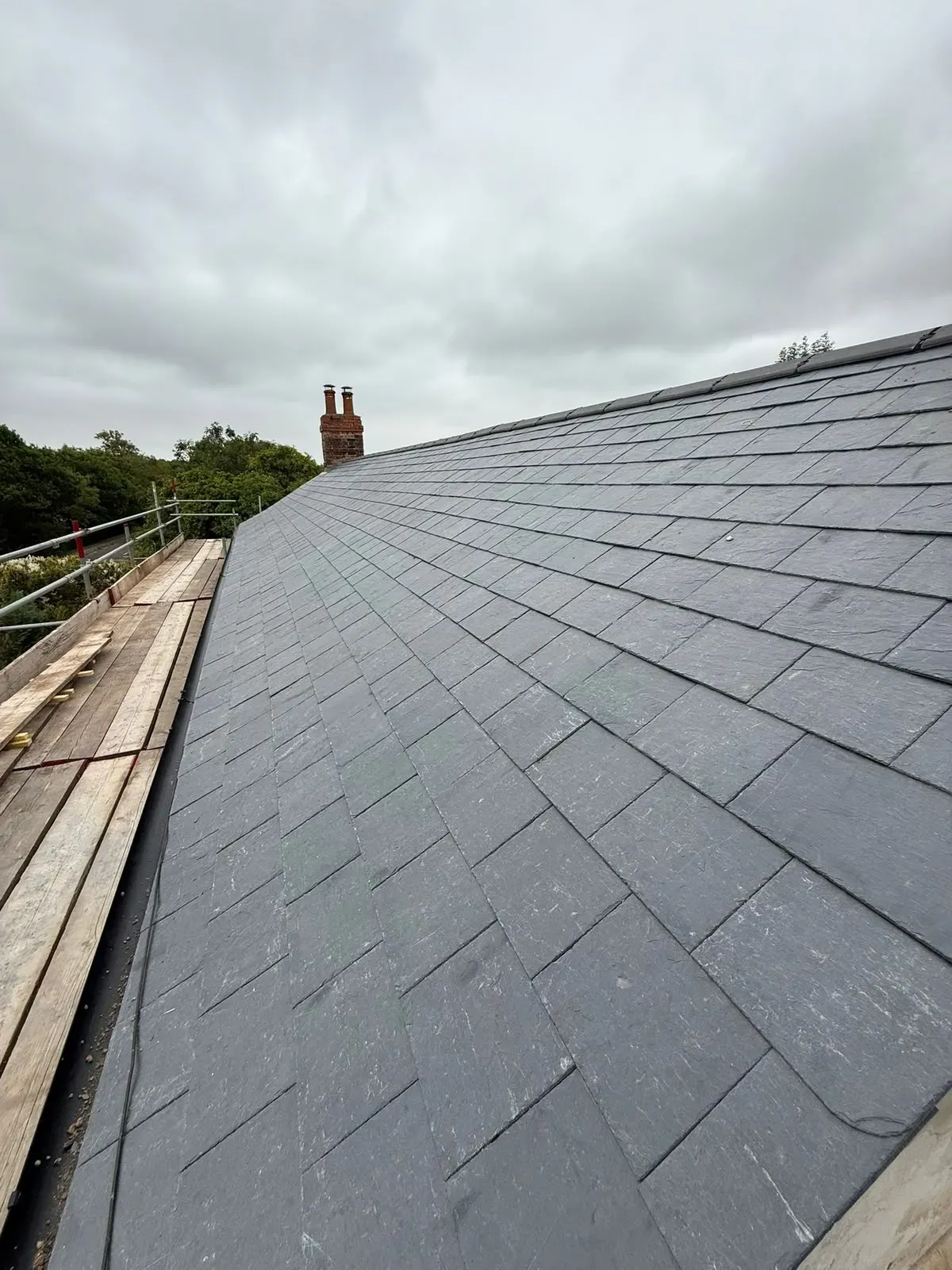 Completed pitched slate roof installation with ridge capping and scaffolding in Worcester