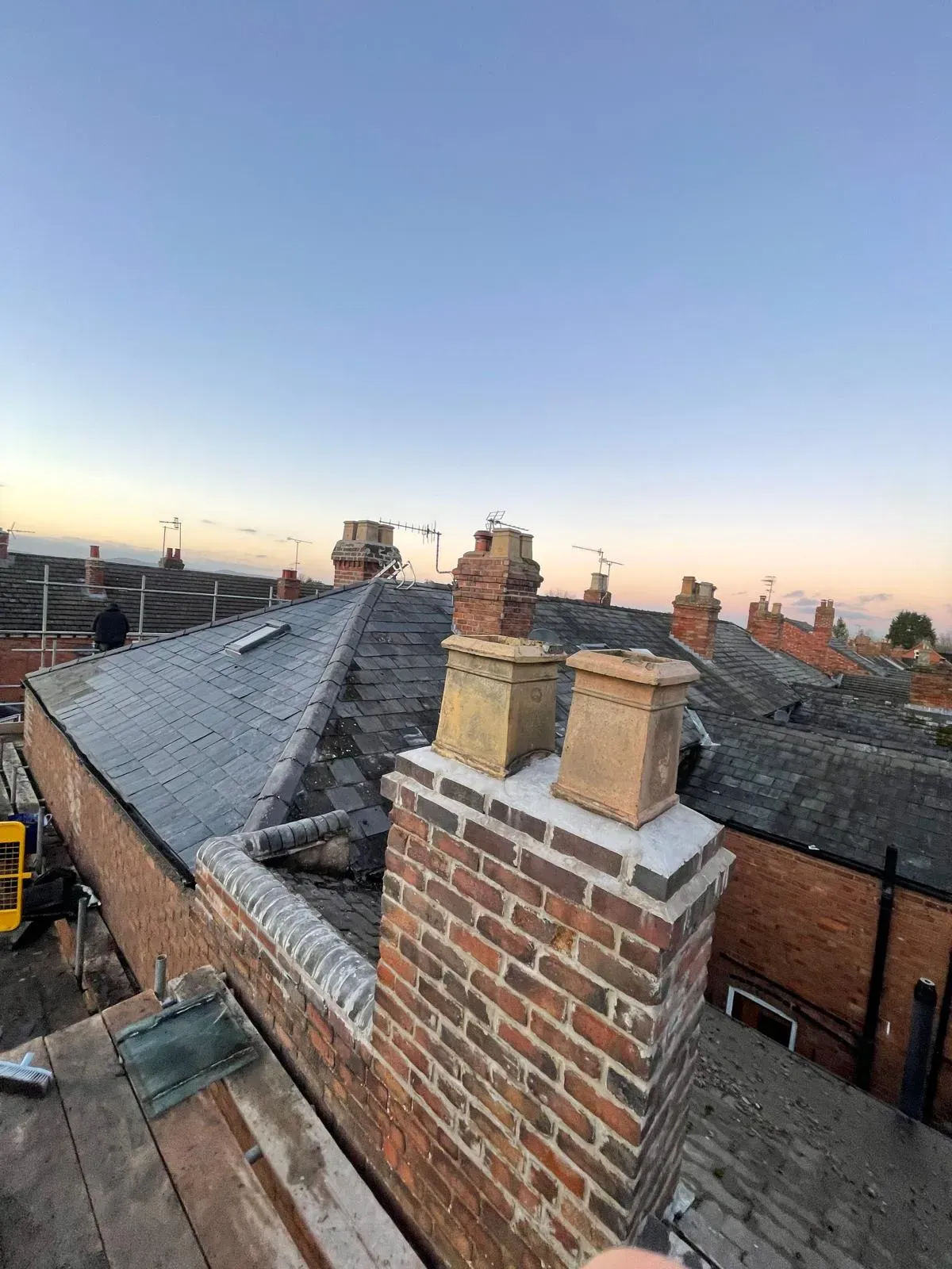 Repointed brick chimney stack with chimney pots and natural slate roof on a terraced house