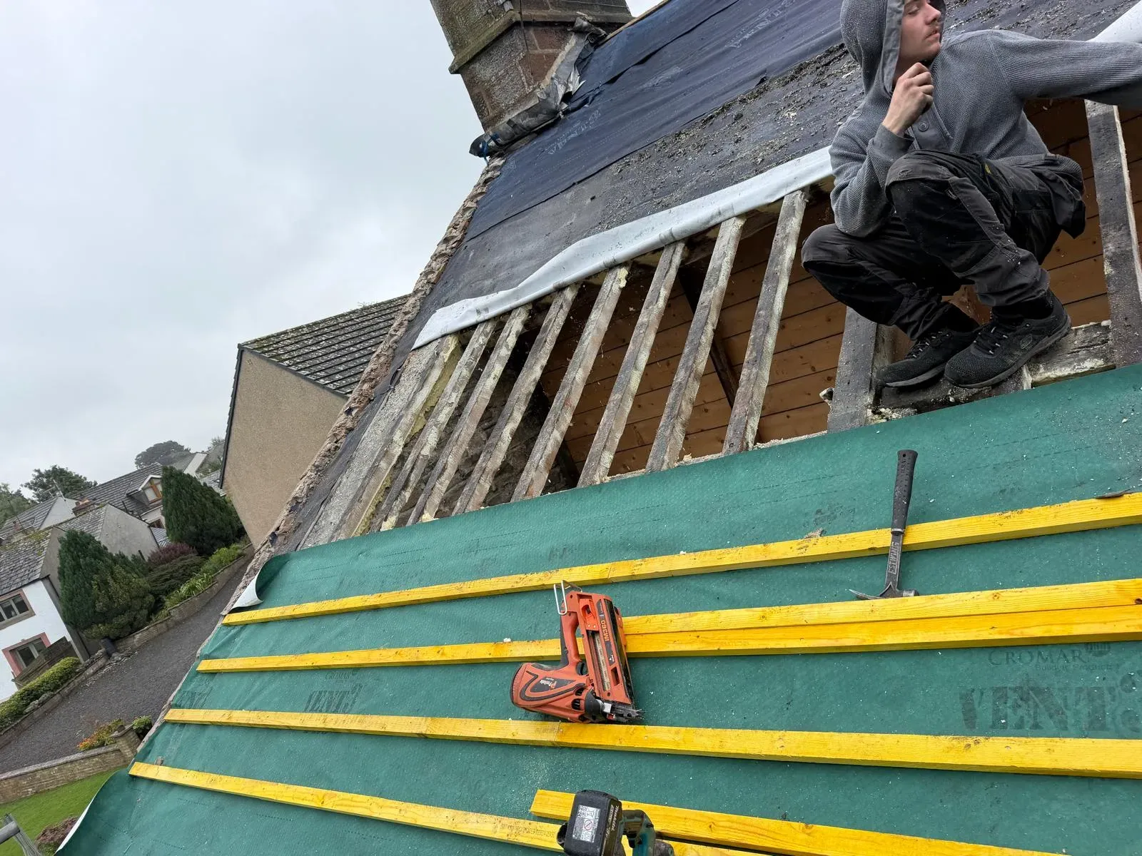 Roofer installing breathable underlay and timber roofing battens on pitched roof rafters