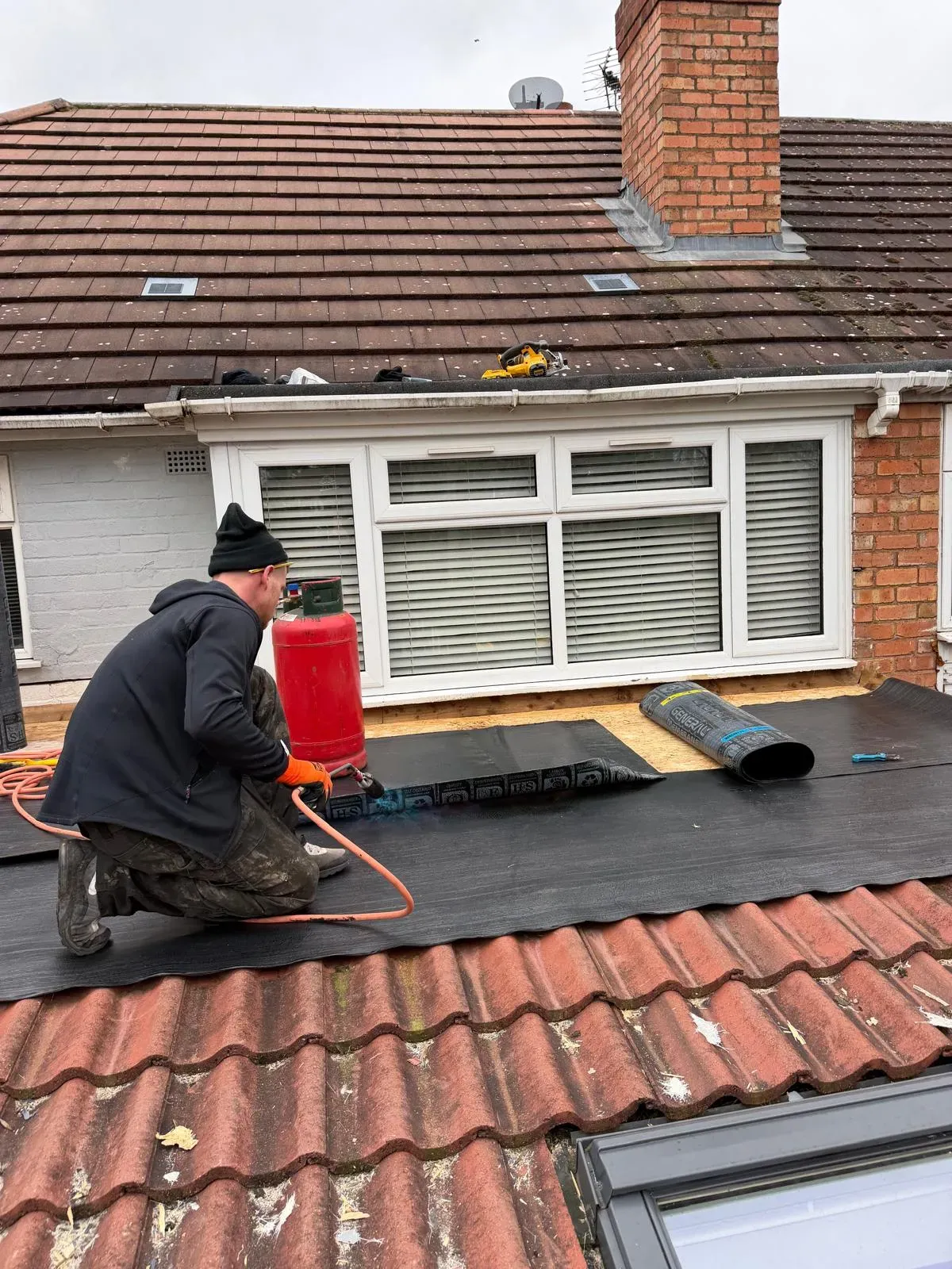 Roofer applying torch-on mineral felt flat roofing membrane on a residential extension in Worcester