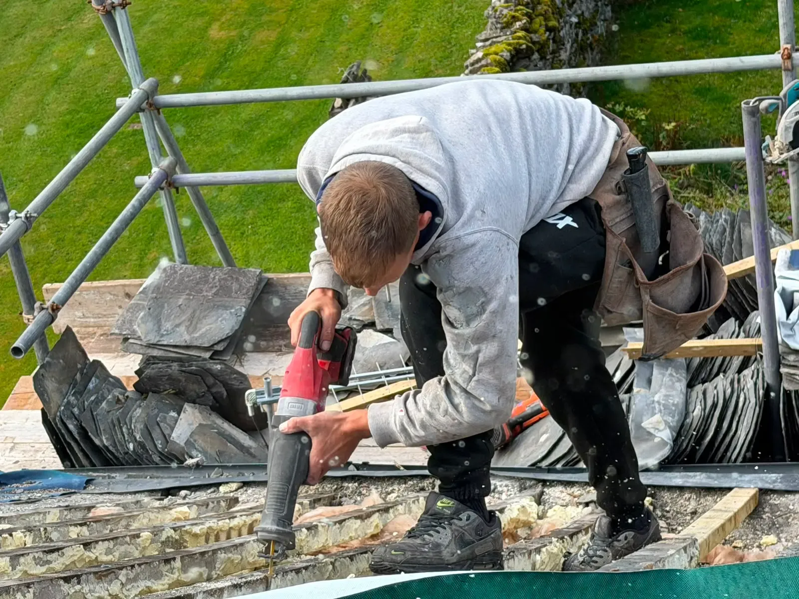 Roofing contractor cutting rafter timbers and clearing insulation on a pitched slate roof restoration