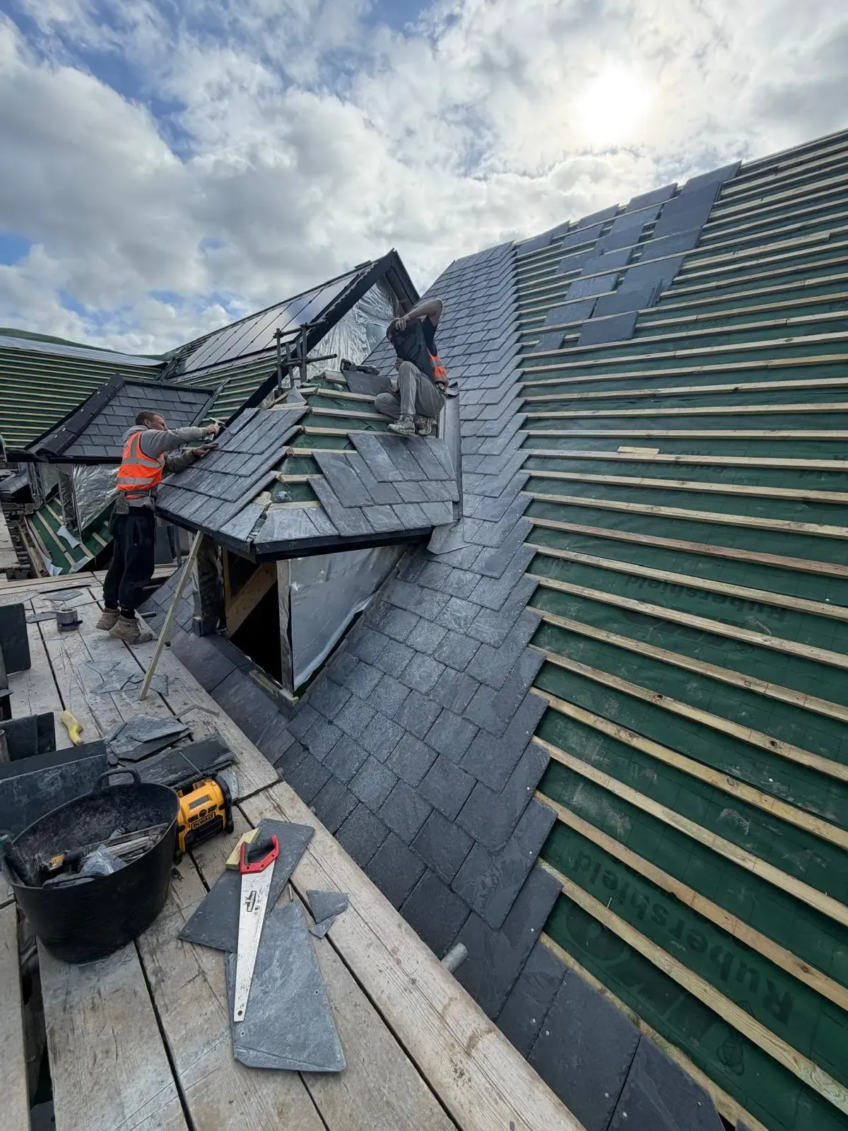 Roofers installing natural slate tiles on timber battens on a pitched dormer roof