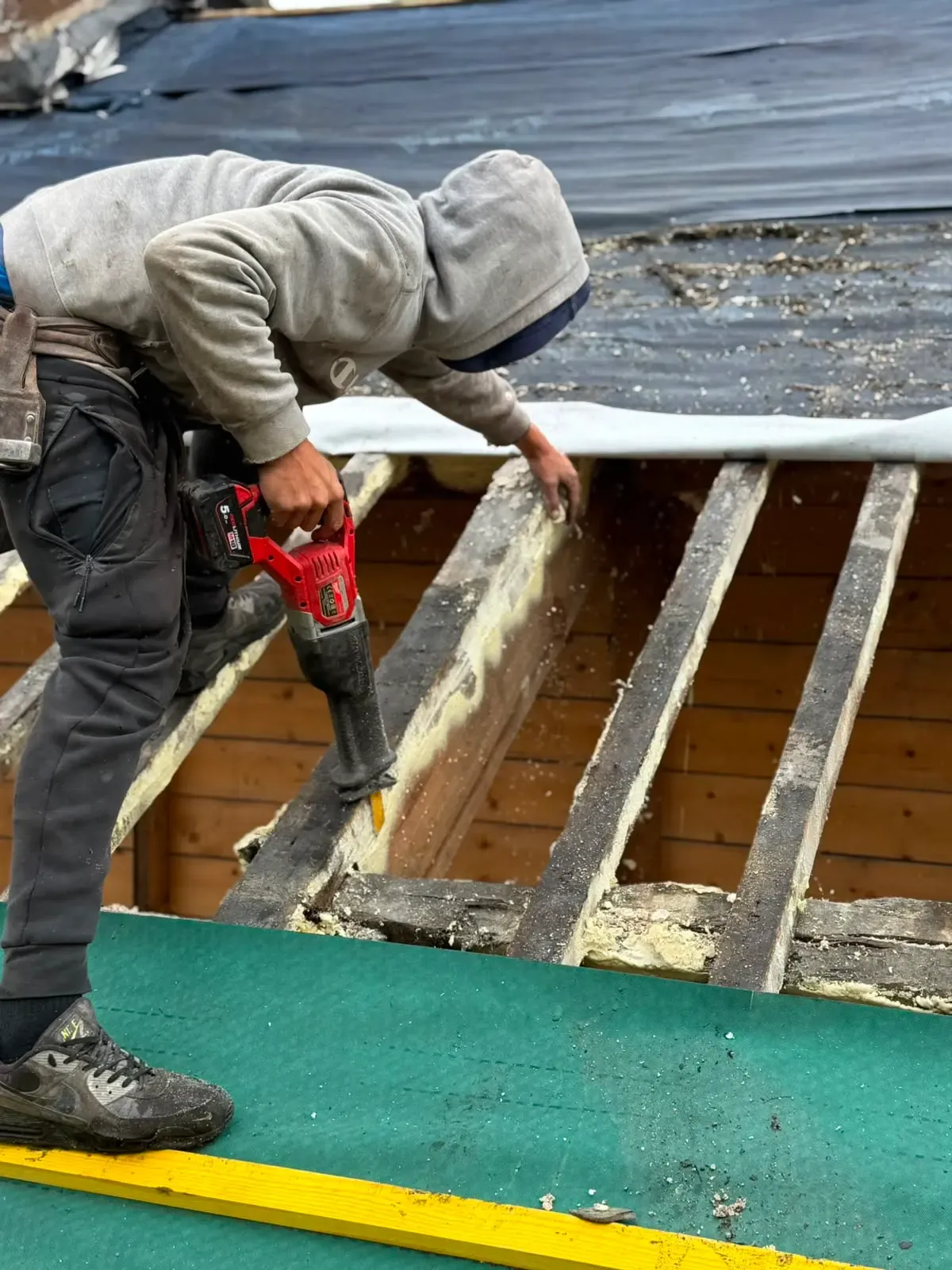 Roofer using a power tool to clear spray foam residue from exposed roof rafters