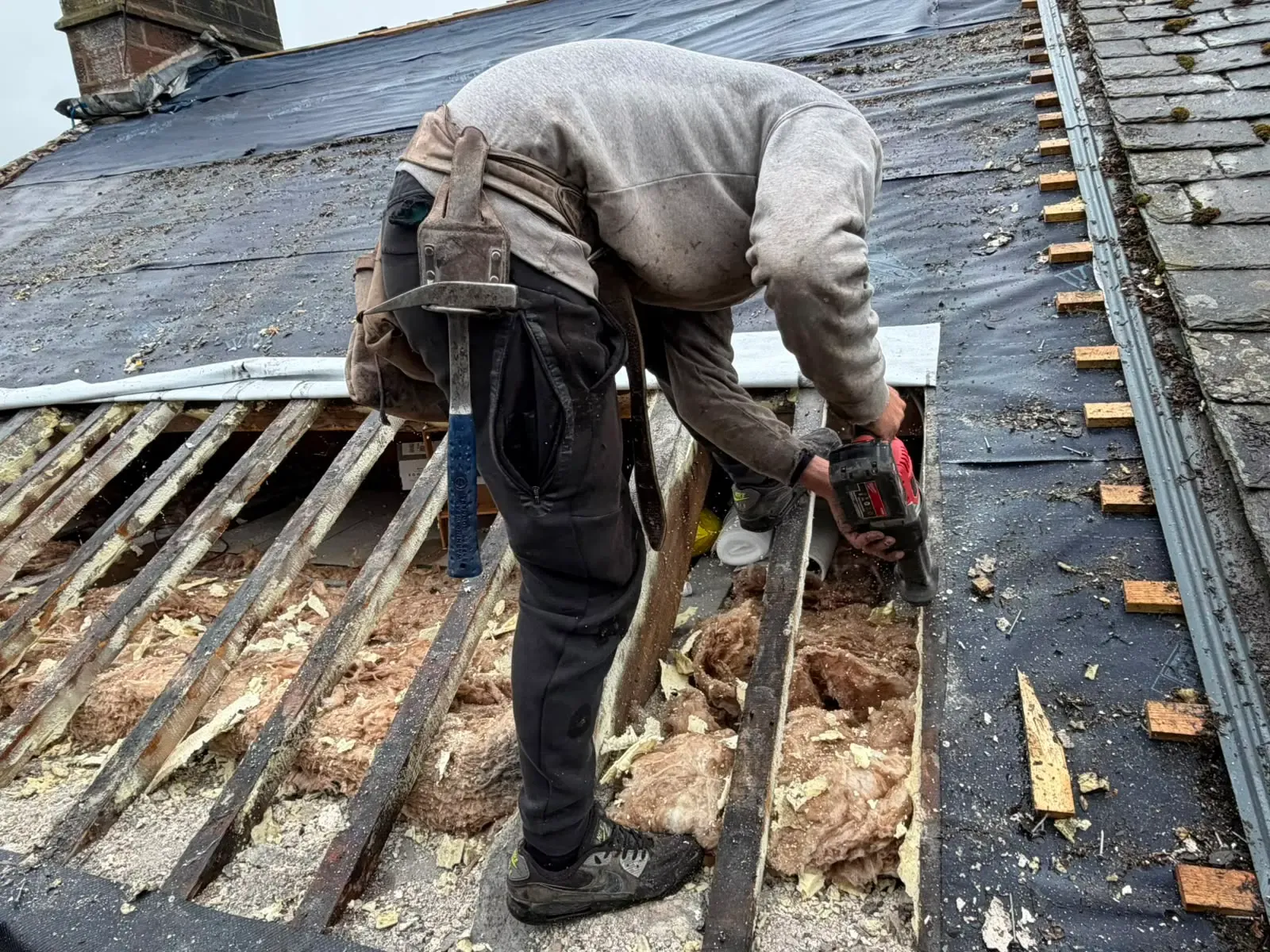 Roofer carrying out timber rafter repairs and insulation removal on a pitched roof in Worcester