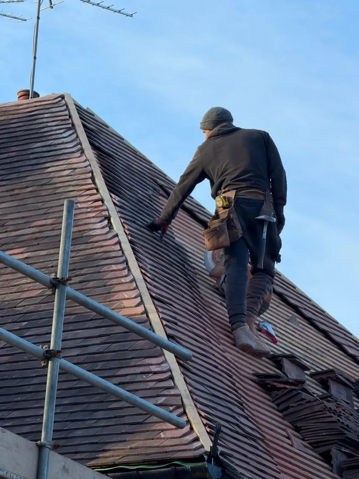 Roofer fitting plain clay tiles on a steep pitched roof structure