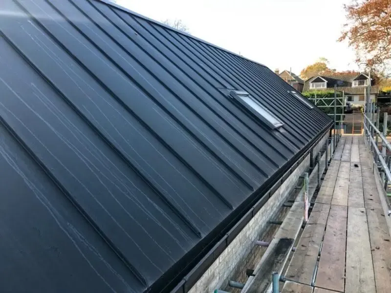 Standing seam metal roof installation with rooflight on a pitched residential property