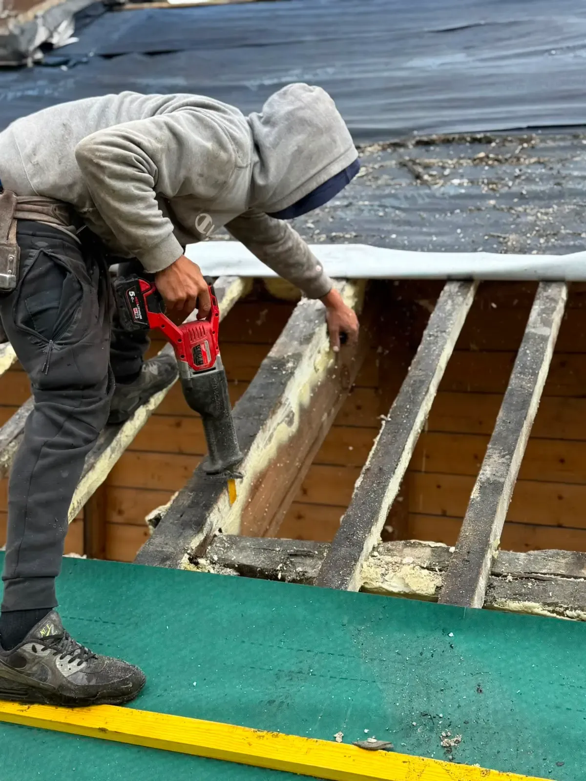 Tradesman carrying out timber repairs and spray foam insulation removal on roof rafters
