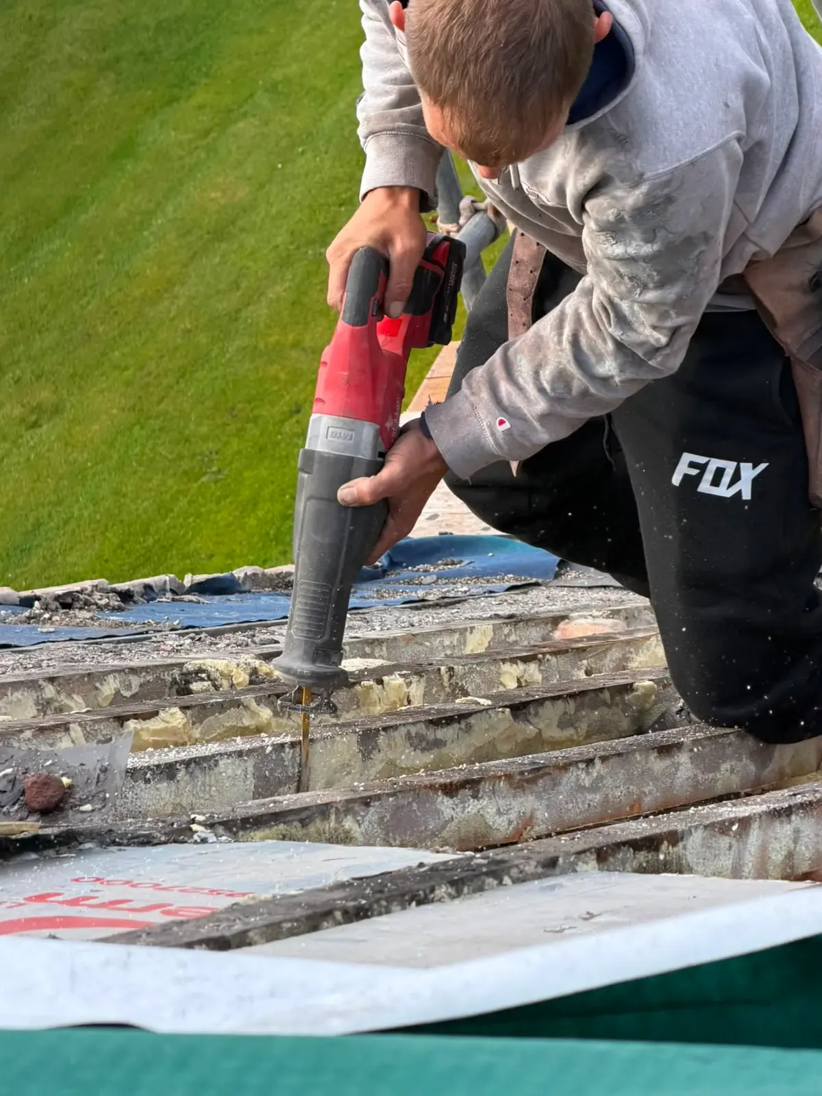 Roofer using a power saw to clear timber rafters during spray foam insulation removal in Worcester