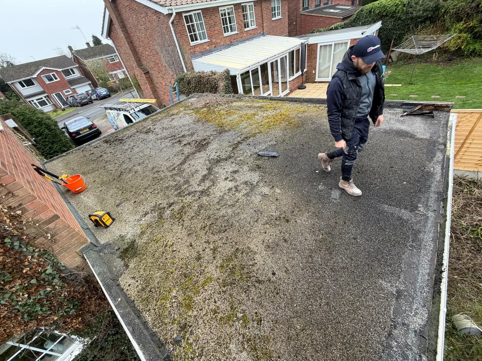 Roofer inspecting a damaged mineral felt flat roof on a residential property in Worcester