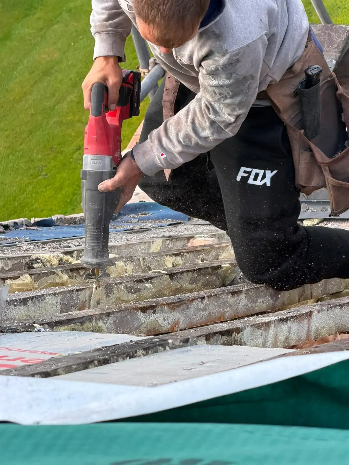 Roofing contractor removing spray foam insulation from between timber roof rafters